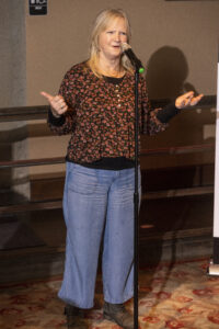 Jean accentuates story using hand gestures. Her left hand is held palm facing up. Her right hand is in a 'thumb's up' position.