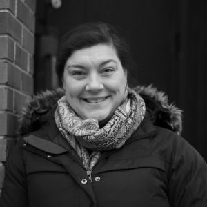 A black and white image of Melissa, who is dressed in a scarf and winter jacket. She is smiling at the camera.