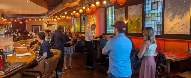 A man in a baseball cap, blue shirt and blue jeans standing next to a woman in a white tank top and pink skirt standing in the entryway next to Sugar Maple's curving bar.