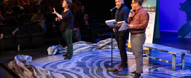 Tom Kerstch and David Lee stand on a stage decorated in a winter snow theme. to the left of both men stands a sign language interpreter.